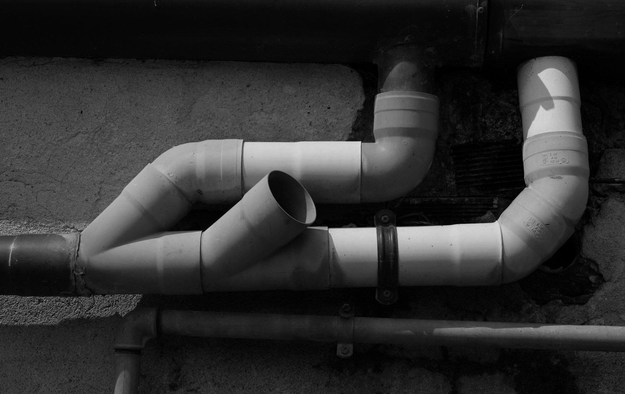 Grey PVC drain pipes and fittings running along a dark concrete wall