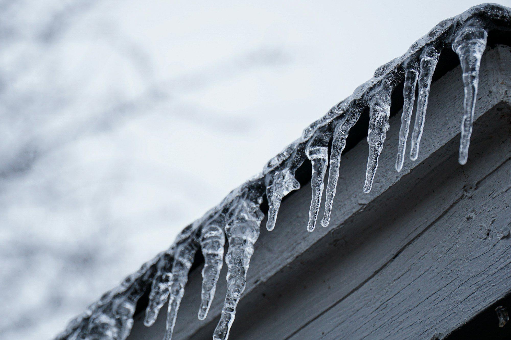 Row of icicles hanging from a snowy roof edge against a pale winter sky