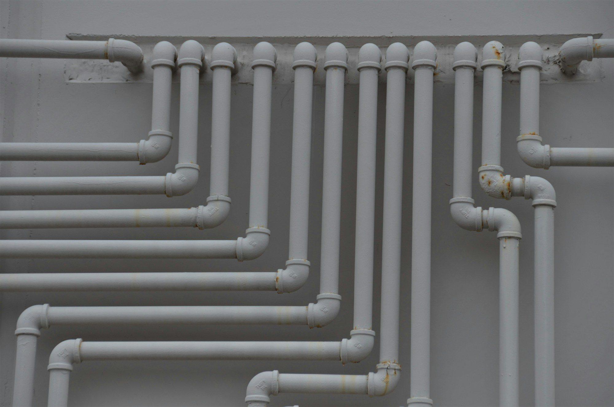 Rows of grey plastic water supply pipes with elbow fittings running along a light wall